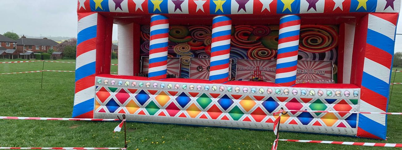 Grand Carnival inflatable stall on an event field, with its marquee-lettered sign, red white and blue pillars and four game bays inside