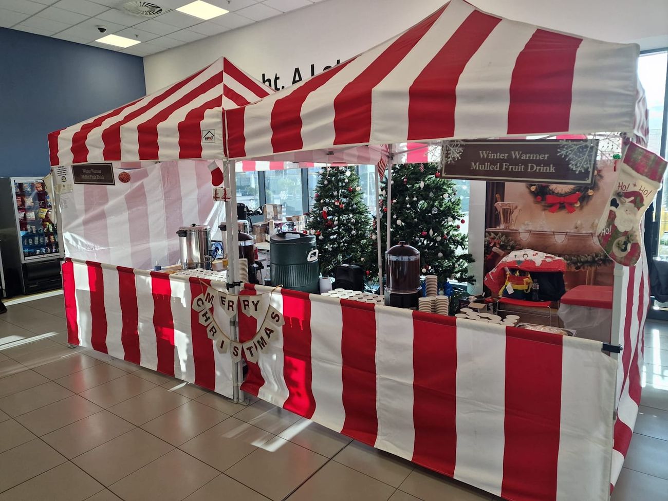 Festive mulled wine stall with its red and white striped canopy at an indoor corporate event