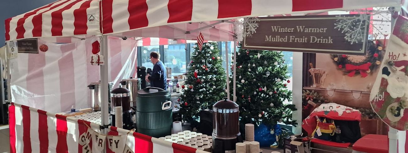 Mulled wine stall set up indoors for a festive event, with striped canopy and serving table