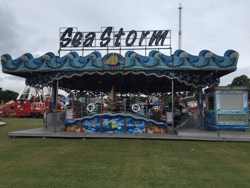 Full Sea Storm family ride set up on grass, with a wave-edged canopy, sea-themed front panels, ride cars and an enclosed booth