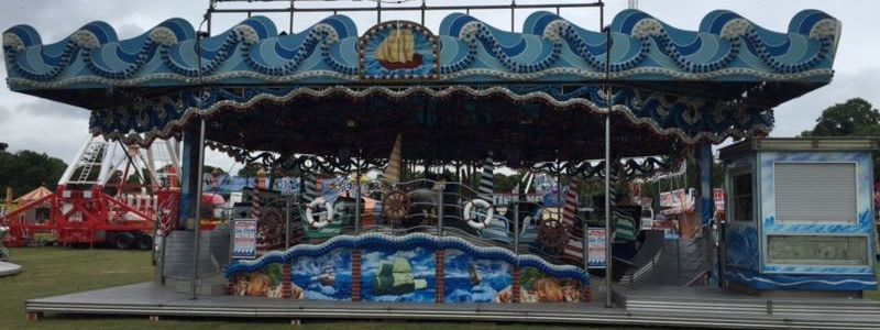 Full Sea Storm family ride set up on grass, with a wave-edged canopy, sea-themed front panels, ride cars and an enclosed booth