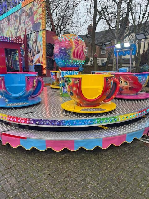 Tea cup ride with character-painted cups on saucers around a central teapot, set up on block paving