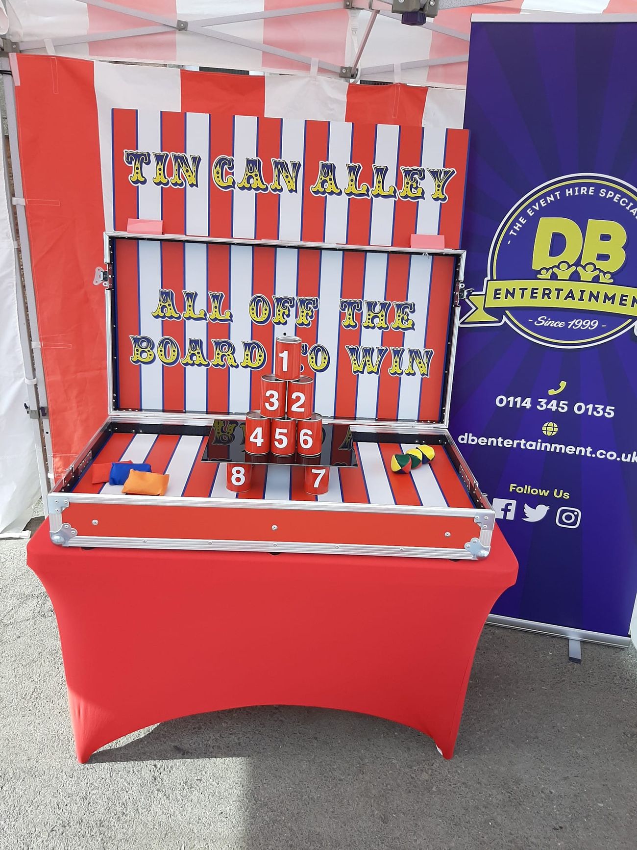 Tin Can Alley stall under its canopy on hard standing, with the numbered cans stacked in a pyramid on the game case