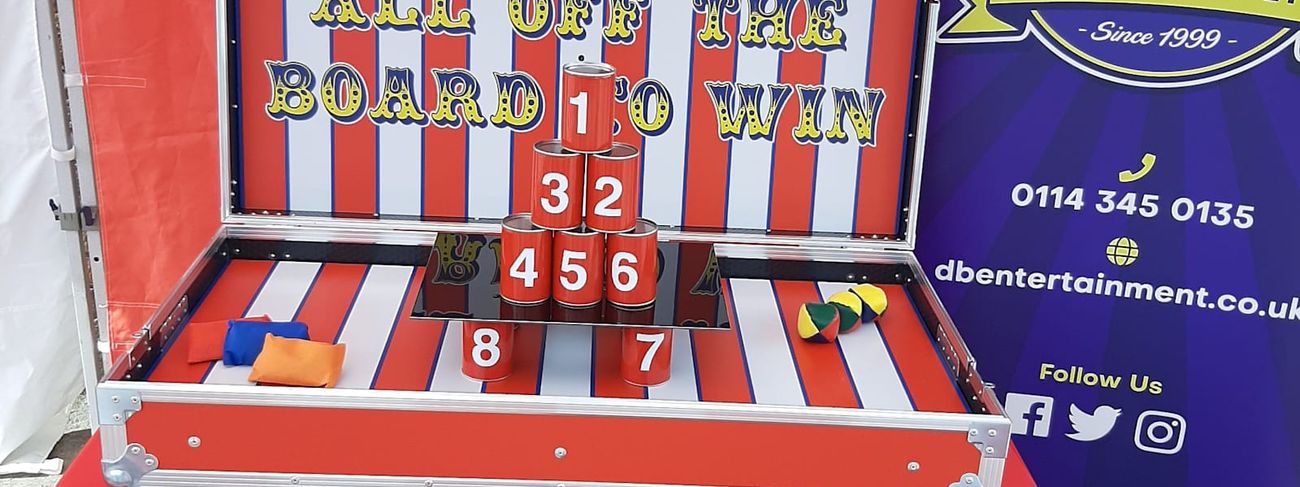 Tin Can Alley stall under its canopy on hard standing, with the numbered cans stacked in a pyramid on the game case