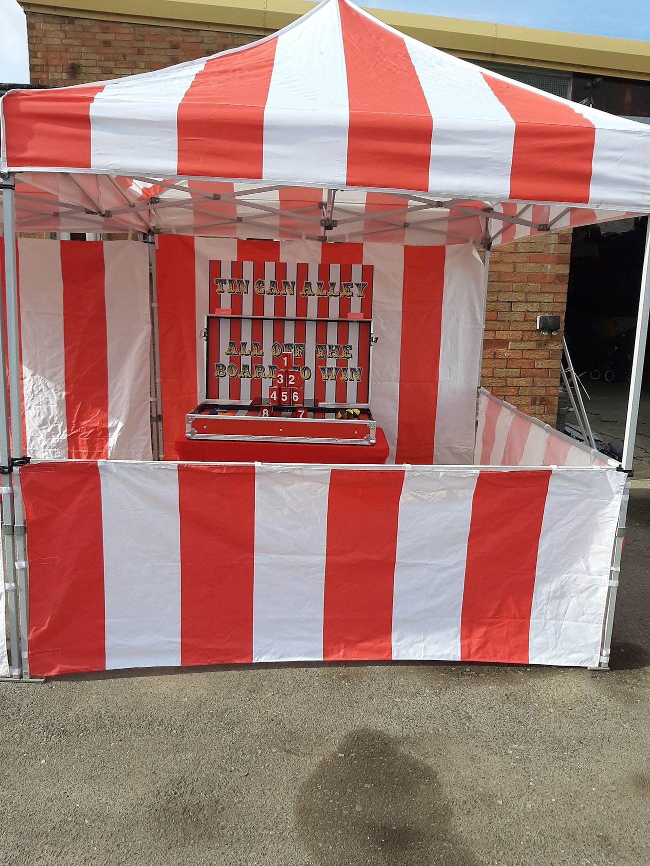 The full striped Tin Can Alley gazebo stall on a paved site, showing the barrier and table layout